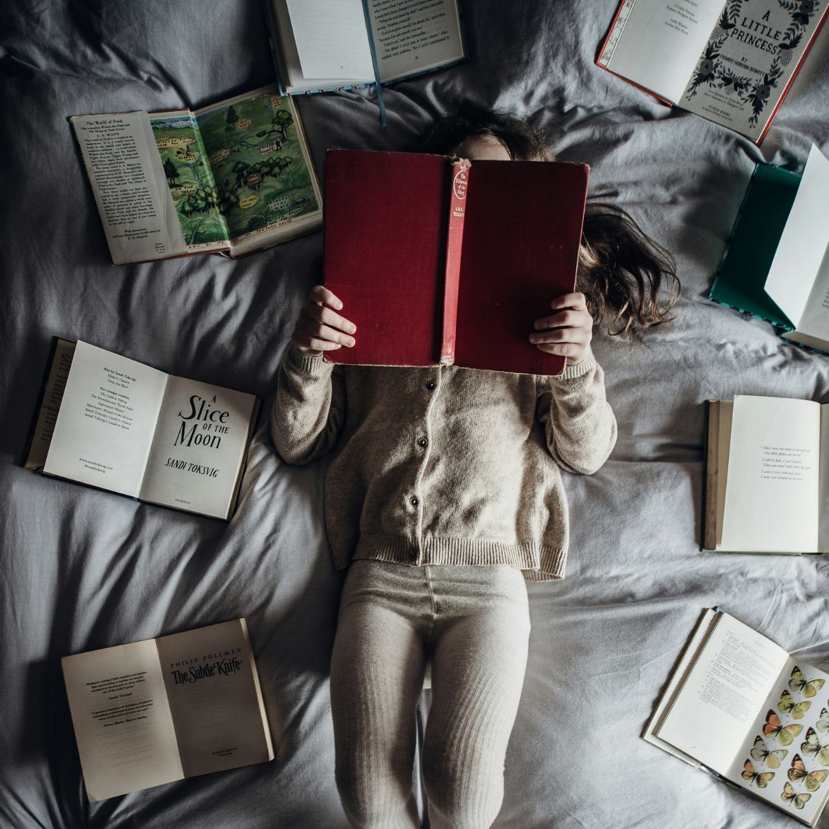 A child reading books on a bed surrounded by books arranged in a circle