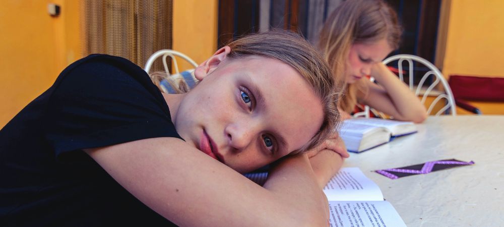 A sleepy school-age child resting her head on an open book